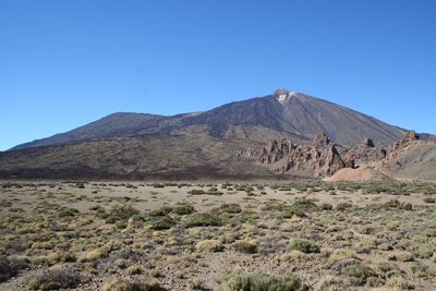Scenic view of arid landscape and mountains against clear blue sky