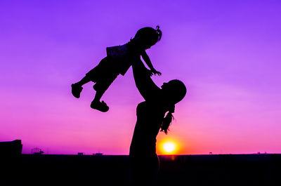 Silhouette mother holding aloft daughter against sky during sunset