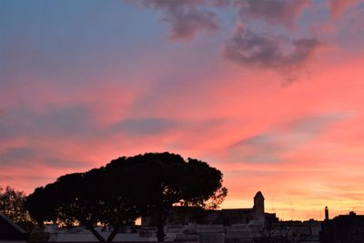 Silhouette trees and buildings against dramatic sky