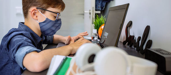 Boy wearing mask studying with laptop at home