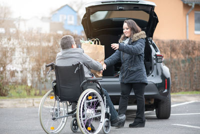 A woman helps aphysical disabled person to get into the car.