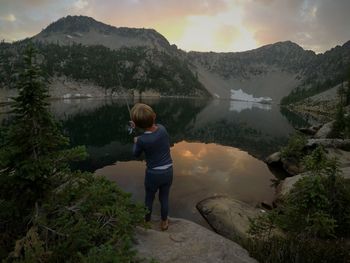 Rear view of child fishing in lake while standing on rock during sunset