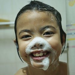 Close-up portrait of smiling girl with soap sud on face in bathroom