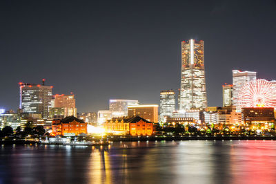 Illuminated buildings by river against sky at night