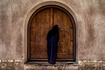 Rear view of veiled woman looking entering through wooden door