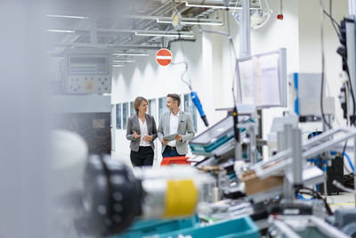 Businesswoman and businessman with tablet walking and talking in a modern factory