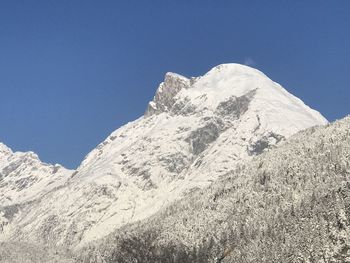 Low angle view of snowcapped mountains against clear blue sky