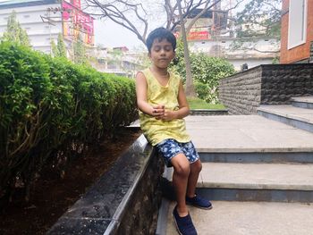 Full length of boy sitting with eyes closed on retaining wall outdoors