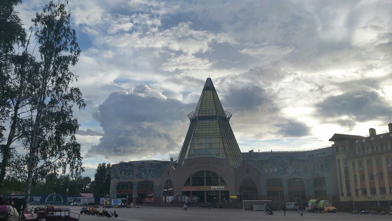 architecture, built structure, building exterior, sky, cloud - sky, car, transportation, land vehicle, street, city, tree, road, incidental people, cloudy, cloud, mode of transport, city life, the way forward, day, travel