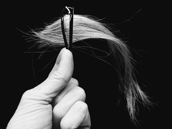 Cropped hand holding clip with hair against black background
