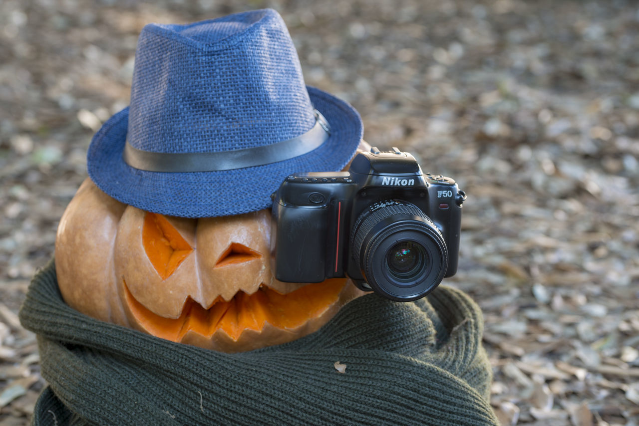 CLOSE-UP OF CAMERA WEARING HAT HOLDING MASK