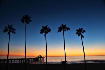 Silhouette palm trees on beach against sky at sunset