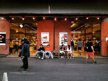 Rear view of people standing on illuminated street at night