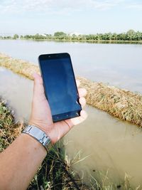 Midsection of person holding smart phone against sky