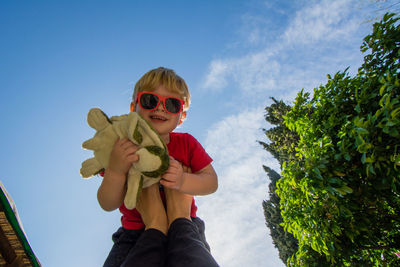 Full length of boy holding sunglasses against sky