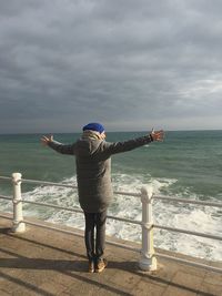 Rear view of woman standing on railing against sea