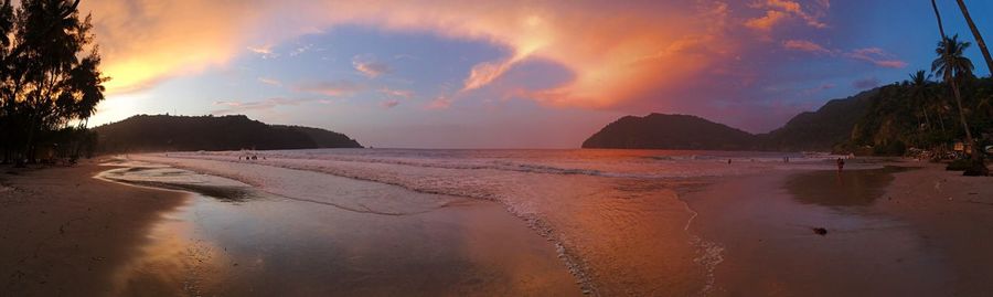 Scenic view of beach against cloudy sky during sunset