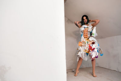 Woman with arms raised standing against white wall