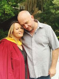 Portrait of woman wearing graduation gown while standing with man on field