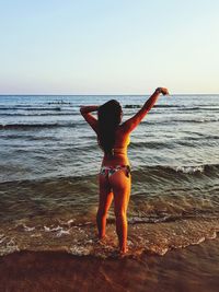 Rear view of woman standing at beach against sky