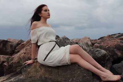 Young woman sitting on rock against sky