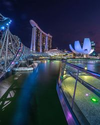 Illuminated bridge over river by buildings in city at night