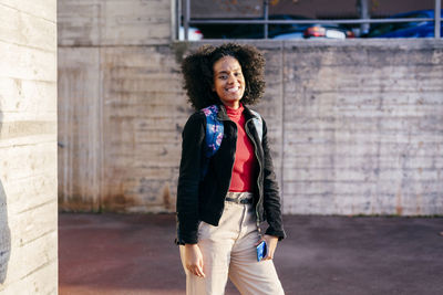 Full length of smiling woman standing against wall