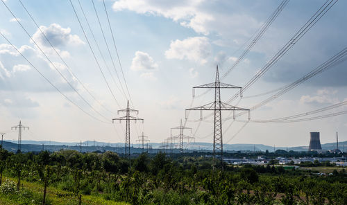 High voltage lines and power pylons in a green landscape, gray sky and chimney of a nuclear power 