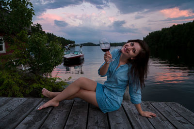 Young woman sitting on wood against sky