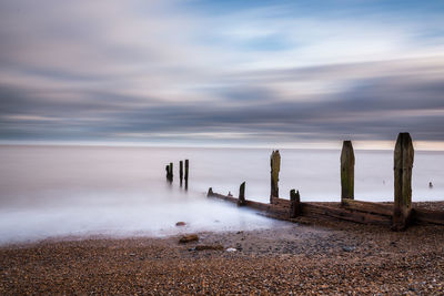 Wooden posts on beach against sky