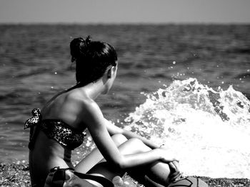 Side view of woman wearing bikini sitting at shore