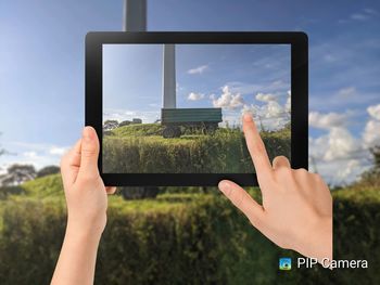 Midsection of person photographing through smart phone against sky