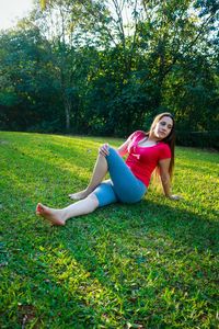 Thoughtful young woman with hand on knee sitting on grassy field at park