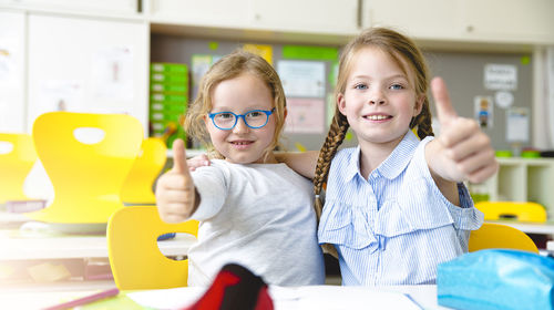 Portrait of cute friends gesturing while studying in classroom