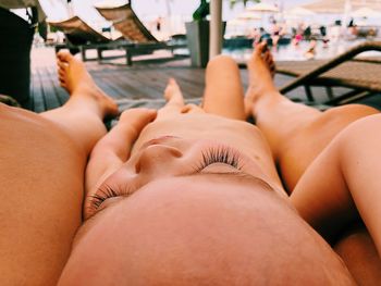 Low section of mother with naked baby boy relaxing at beach