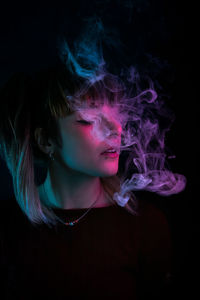 Young woman smoking against black background