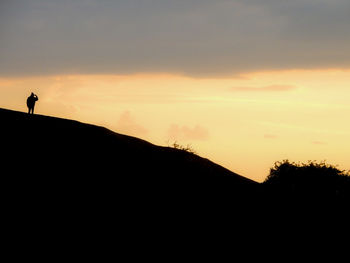 Silhouette man standing on mountain against sky during sunset