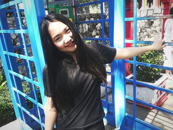 Portrait of smiling woman standing against blue telephone booth