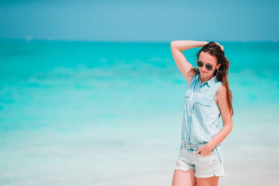 Young woman wearing sunglasses standing by sea against sky