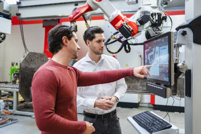 Engineer explaining colleague through computer at industry