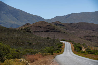 Road leading towards mountains against clear sky