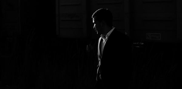 Silhouette of young man in the classic suit looking away with harsh backlighting