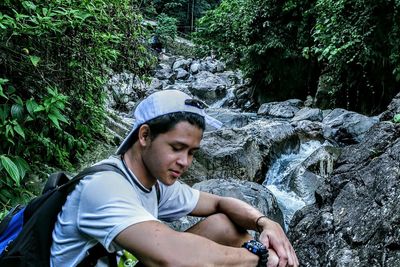 Young man looking away while standing on rock in forest