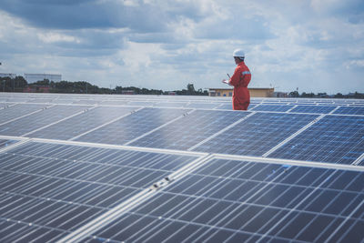 Engineer standing amidst solar panel against cloudy sky