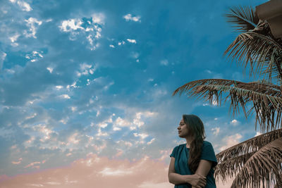 Low angle view of woman looking at tree against sky