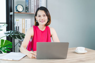 Portrait of smiling woman using phone while sitting on table