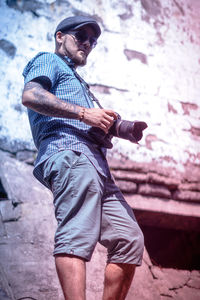 Man holding camera while standing against wall