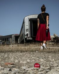 Rear view of woman walking by abandoned train coaches on field