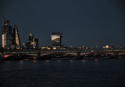 Illuminated bridge over river against buildings at night