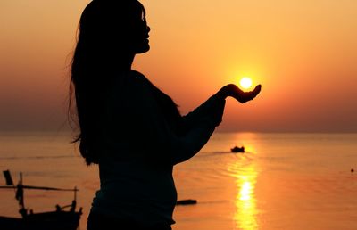 Silhouette woman holding sun by sea during sunset